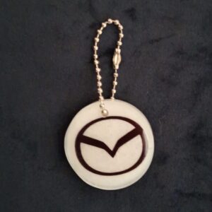 Een witte sleutelhanger met het logo van automerk Mazda met een zilverkleurig kettinkje.