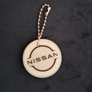 Een witte ronde sleutelhanger met het logo van automerk Nissan met een zilverkleurig kettinkje.